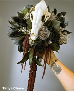 a hand holding a bouquet with flowers and a cow's skull on top of it