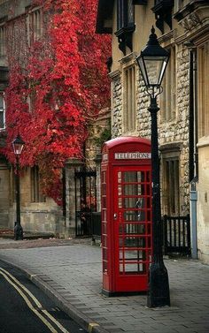 a red phone booth sitting on the side of a road next to a lamp post