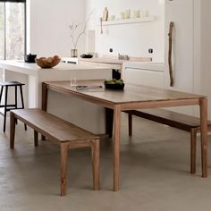 a wooden table sitting next to a white counter top in a kitchen with two stools