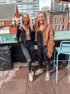 two women standing next to each other on top of a roof with buildings in the background