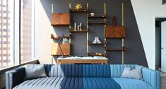 a blue couch sitting in front of a window next to a wooden shelf filled with books