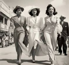 three women walking down the street in suits and hats