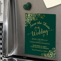 a green and gold wedding save the date card on top of a refrigerator freezer