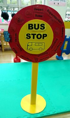 a red bus stop sign sitting on top of a yellow stand