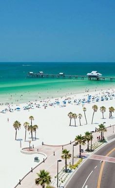 an aerial view of a beach with palm trees and blue umbrellas in the foreground