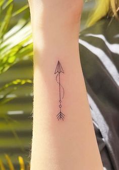 a small arrow tattoo on the left wrist is shown in black ink, and has an arrow