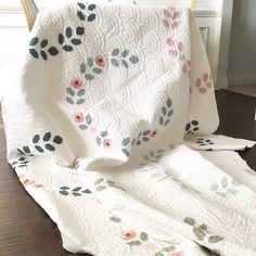 a white quilt with pink and green flowers on it sitting on top of a wooden floor