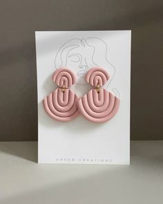 a pair of pink earrings sitting on top of a white card next to a gray wall