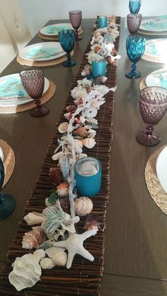 the table is set with blue glassware and seashells on top of it