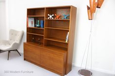 a white chair sitting in front of a wooden book shelf next to a wall mounted lamp