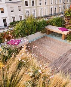 a wooden deck surrounded by lots of plants and flowers in front of white building with balconies