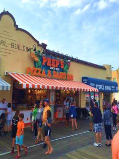 many people are walking around in front of a pizza and dairy shop on the boardwalk