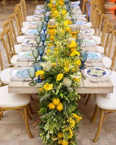 a long table with yellow flowers and blue dishes on it is set for a formal dinner