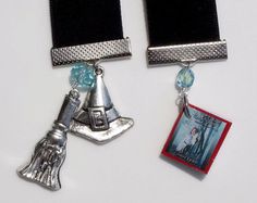 two black and silver bookmarks with charms attached to them on a white table top