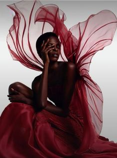 a woman in a red dress sitting on the ground with her hands to her face