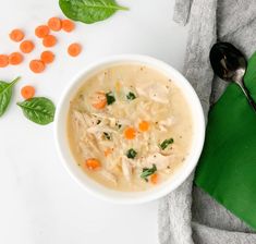 a white bowl filled with chicken and carrots on top of a green napkin next to a spoon