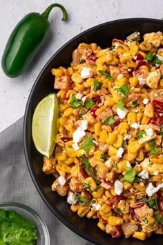 a black bowl filled with corn salad next to a green pepper and lime wedges