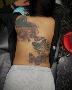 a woman with a butterfly and rose tattoo on her upper back side ribcage