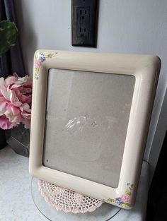 an old photo frame sitting on top of a table next to pink flowers and a black light switch