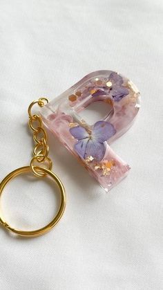 a gold keychain with a pink and purple flowered letter charm hanging from it's side