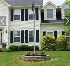 a large white house with black shutters and flowers in the front yard on a sunny day