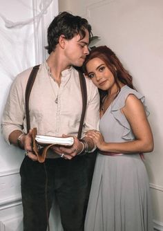 a man and woman standing next to each other in front of a white wall with curtains