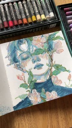 a drawing of a woman's face with flowers in her hair and watercolors next to it