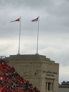 an american flag flying in front of a stadium full of people