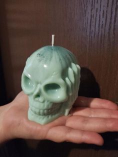 a hand holding a green skull candle in it's palm