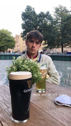 a young man sitting at a table with a beer and flowers in front of him