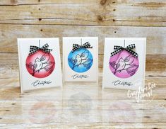 three cards with christmas ornaments on them sitting next to each other in front of a wooden background