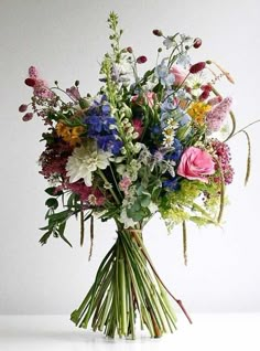 a vase filled with lots of colorful flowers on top of a white table next to a wall