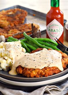 a plate topped with meat covered in gravy next to green beans and mashed potatoes