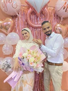 two people standing next to each other in front of balloons and streamers with flowers