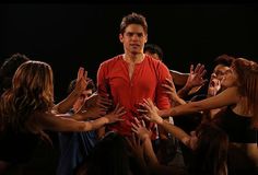 a group of people standing around each other with their hands in the air and one man wearing a red shirt