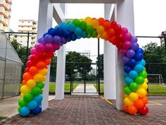 a rainbow colored arch with balloons attached to it in the middle of a brick walkway