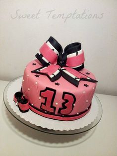 a pink birthday cake decorated with black and white ribbons on a glass platter that says sweet temptationions