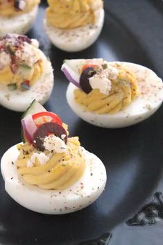 several deviled eggs with various toppings on a black plate, ready to be eaten