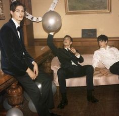 two men in suits are sitting on a couch and one man is holding a balloon