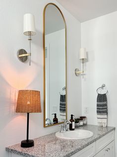 a bathroom sink with a large mirror above it and a lamp on the counter next to it