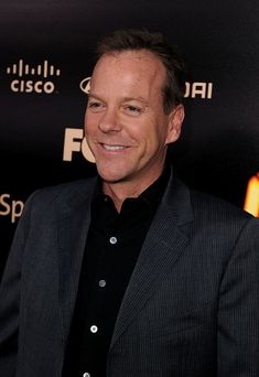 a man in a black shirt and suit smiling at the camera with his hand on his hip