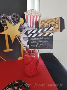 a red table topped with a mason jar filled with popcorn and movie clapper sticks