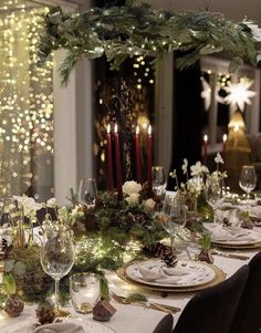 a table set for christmas dinner with candles and greenery in the centerpieces