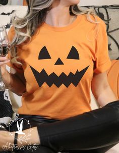 a woman sitting on a couch holding a wine glass in her hand and wearing an orange halloween t - shirt