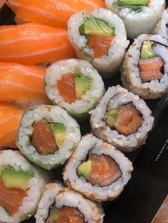 several sushi rolls are arranged on a black platter with carrots and avocado