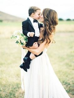 a woman in a white dress holding a young boy wearing a tuxedo and bow tie