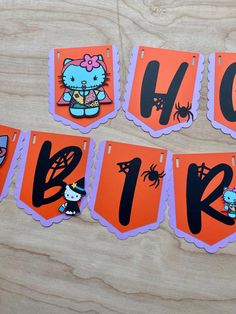 hello kitty halloween banner hanging on a wooden table with orange and purple paper cutouts