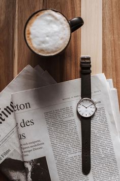 a watch sitting on top of a newspaper next to a cup of coffee