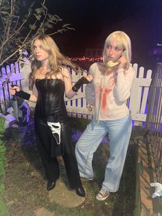 two women dressed up as zombies in front of a white picket fence at night time