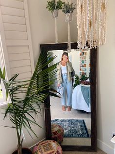 a woman standing in front of a mirror next to a plant and potted plant